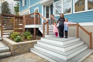 mother standing with two young daughters on renovated porch on blue house