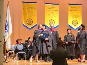 graduate in cap and gown posing with dean on stage