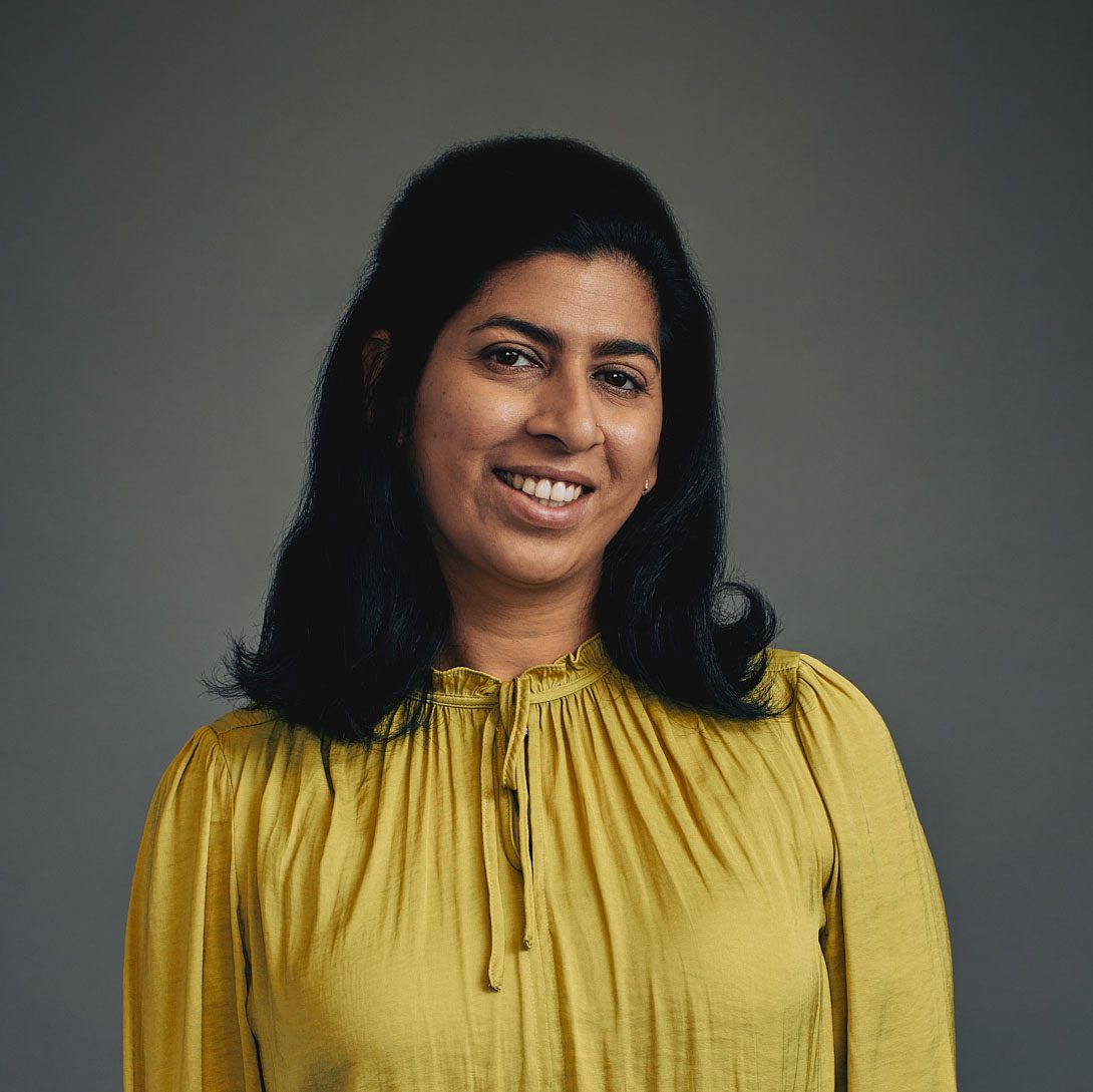 Woman smiling at camera with dark hair and mustard-colored shirt.