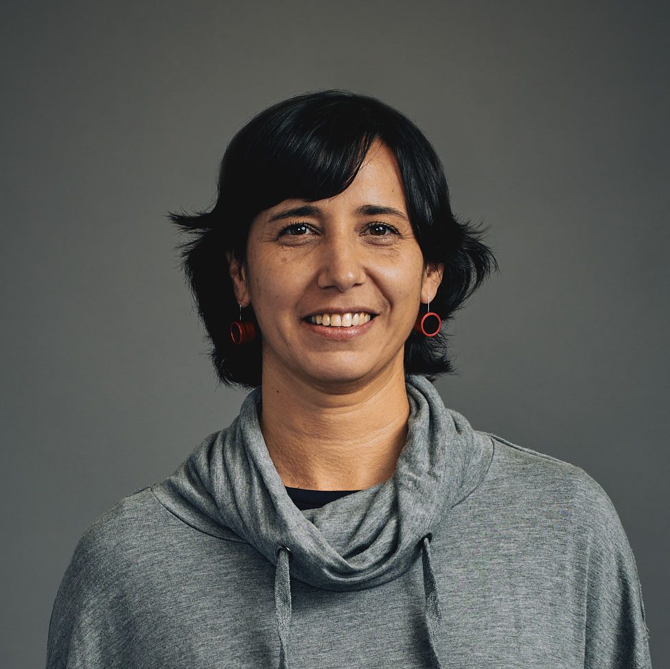 Woman smiling wearing a gray cowled shirt.